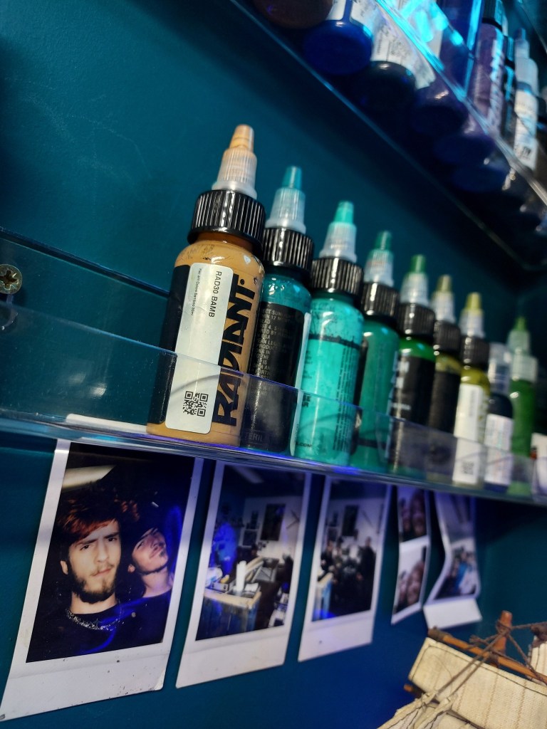 Tattoo inks, teal walls, polaroid photos underneath.
